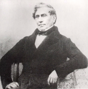 Formal photograph of a man sitting in a posed manner.  He is dressed in formal jacket and bow tie.